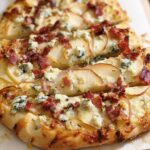 Close-up of a 10-ingredient pizza topped with pear slices, crumbled blue cheese, and crispy bacon.
