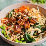 A vibrant and delicious 20-Ingredient Rice Bowl featuring crispy tofu, edamame, broccoli, carrots, noodles, and a creamy sauce.
