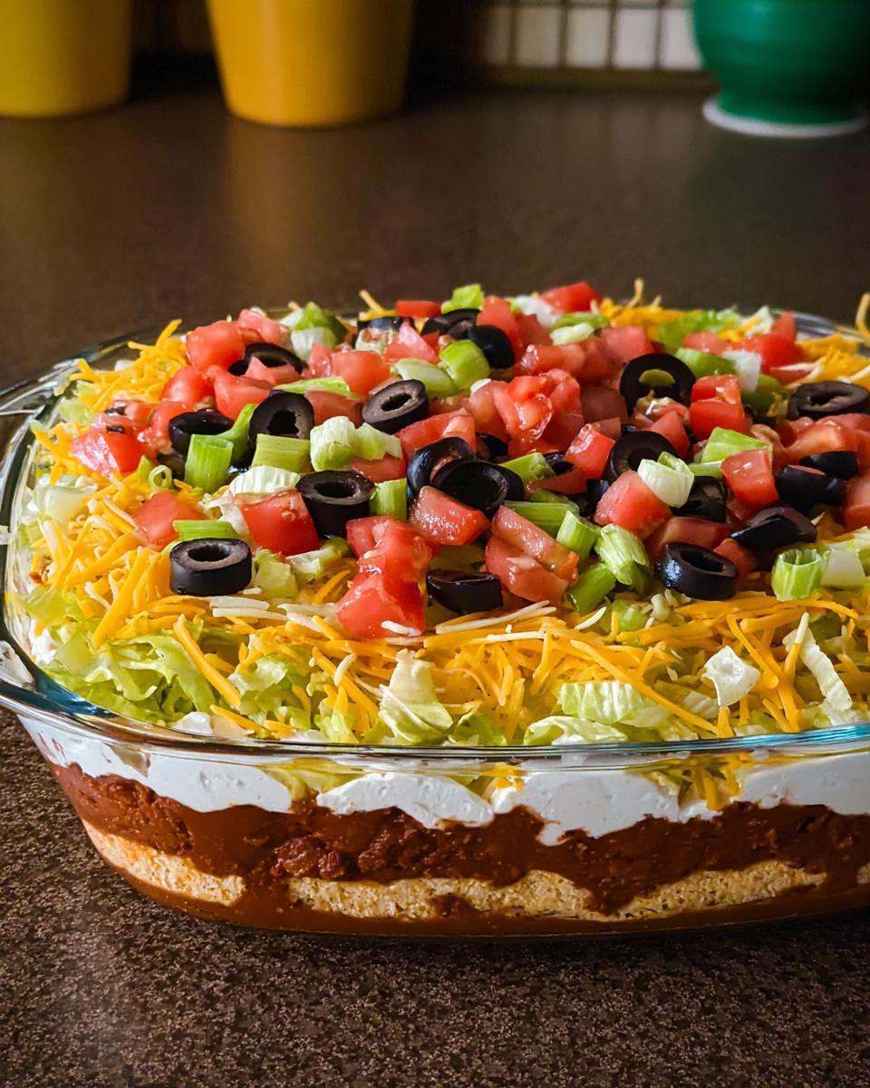 A delicious 7-layer taco dip, perfect for Taco Tuesday recipes, topped with tomatoes, olives, cheese, and lettuce.
