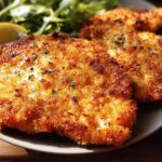 Close-up of golden-brown, crispy air fryer chicken breasts served with a lemon wedge and salad.