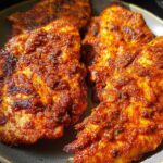 Close-up of air fryer chicken recipes, featuring juicy chicken breasts coated in a vibrant red spice rub.