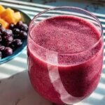 A vibrant berry smoothie in a glass, next to a bowl of fresh blueberries and melon chunks. Perfect for breakfast ideas recipes.