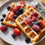 Golden brown waffles topped with fresh raspberries, blueberries, and strawberries, dusted with powdered sugar. A perfect breakfast idea recipe.
