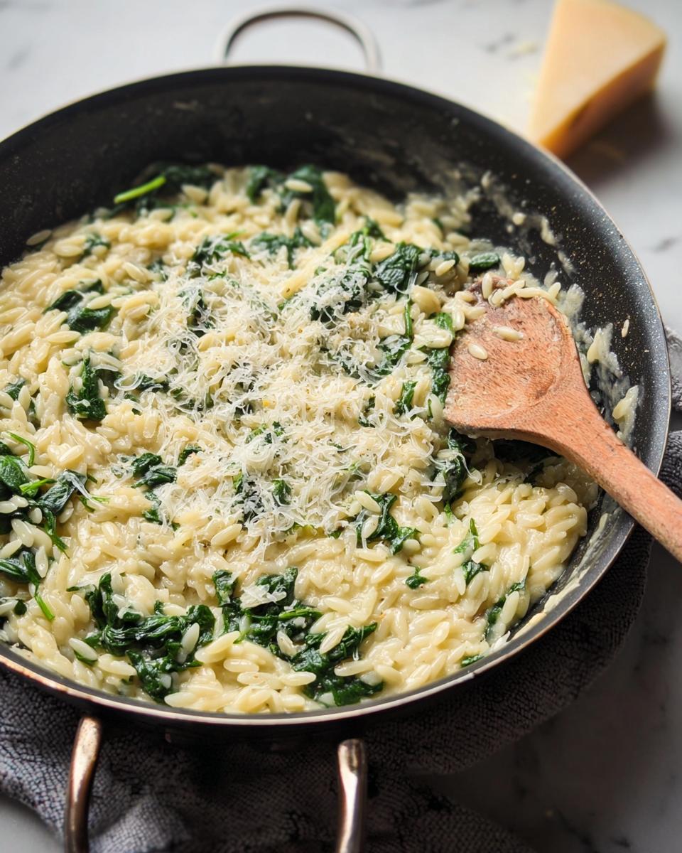 Close-up of creamy spinach orzo in a pan, topped with grated parmesan cheese and a wooden spoon.