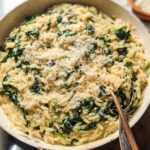 Close-up of creamy spinach orzo pasta dish in a pan, topped with grated parmesan cheese. A perfect veggie sides recipe.