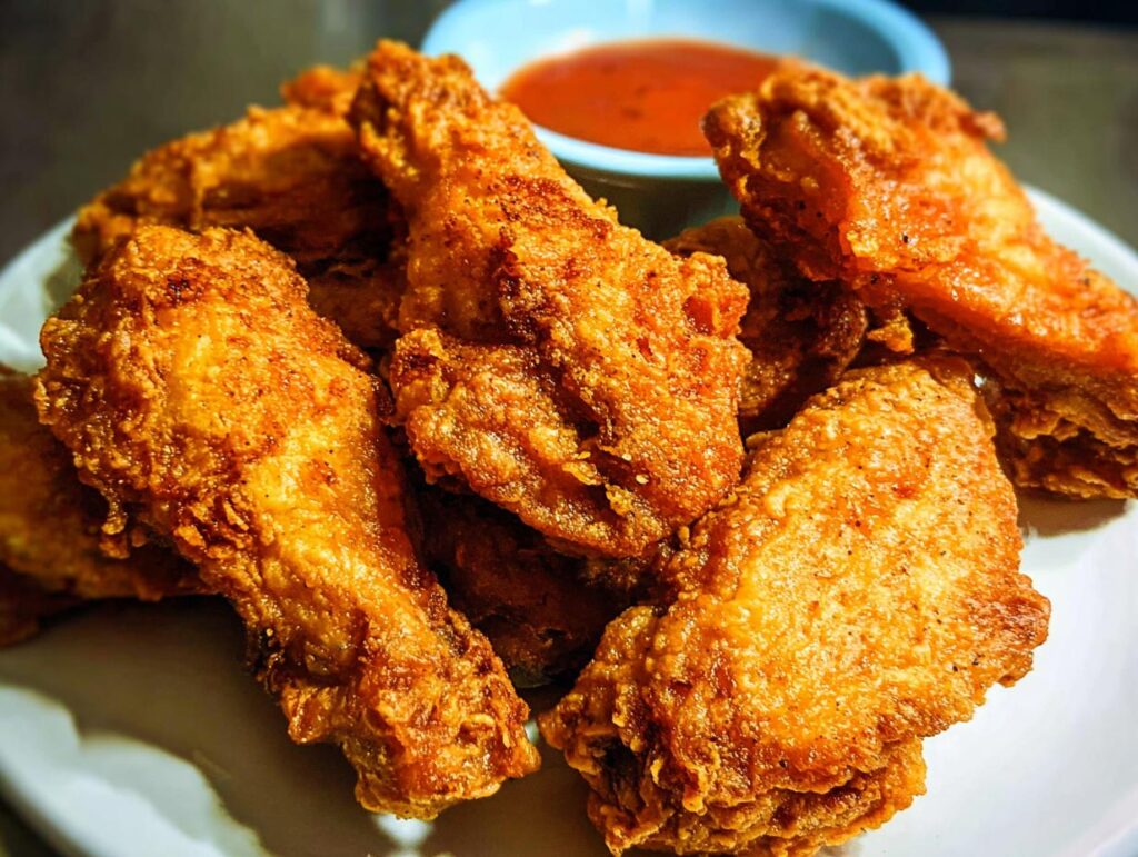 A pile of golden-brown, crispy fried chicken wings served with a side of dipping sauce.