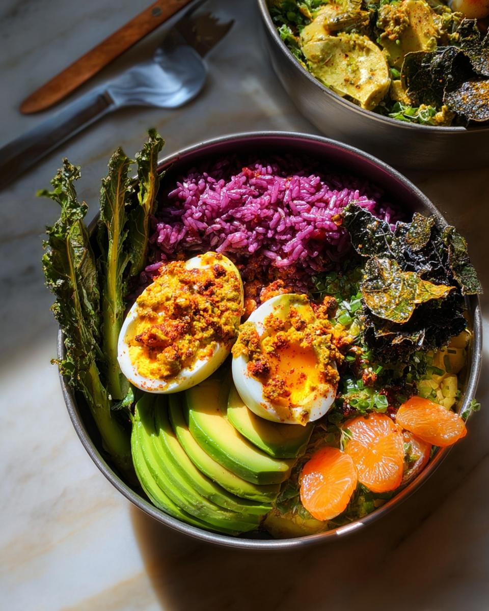 Close-up of a bowl featuring two halves of deviled eggs, purple rice, sliced avocado, and greens, part of The Ultimate Egg Recipes Guide for Beginners.