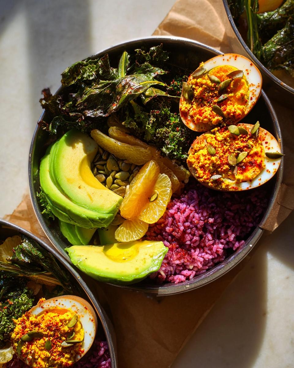 A vibrant egg bowl featuring halved hard-boiled eggs, avocado slices, oranges, purple rice, and kale.