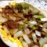 Close-up of a breakfast burrito filled with scrambled eggs, seasoned ground meat, diced onions, and green peppers.