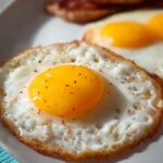 Close-up of a perfectly fried egg with a bright yellow yolk, seasoned with pepper. A great egg recipe.