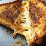 A close-up of a perfectly grilled cheese recipe, cut in half with gooey cheese stretching out.