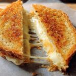 A perfectly grilled cheese sandwich, cut in half, with melted cheese oozing out, showcasing one of the best grilled cheese recipes.