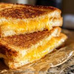 A close-up of two perfectly golden-brown grilled cheese sandwiches stacked, with melted cheese oozing out.