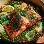 A healthy meal featuring a salmon fillet served over lentils with peas and fennel, garnished with dill and lemon.