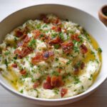 A bowl of creamy mashed potatoes topped with crispy bacon bits and fresh parsley.