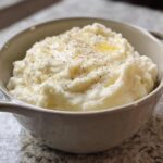 A bowl of fluffy mashed potatoes, topped with melted butter and cracked black pepper, perfect for meal prep.