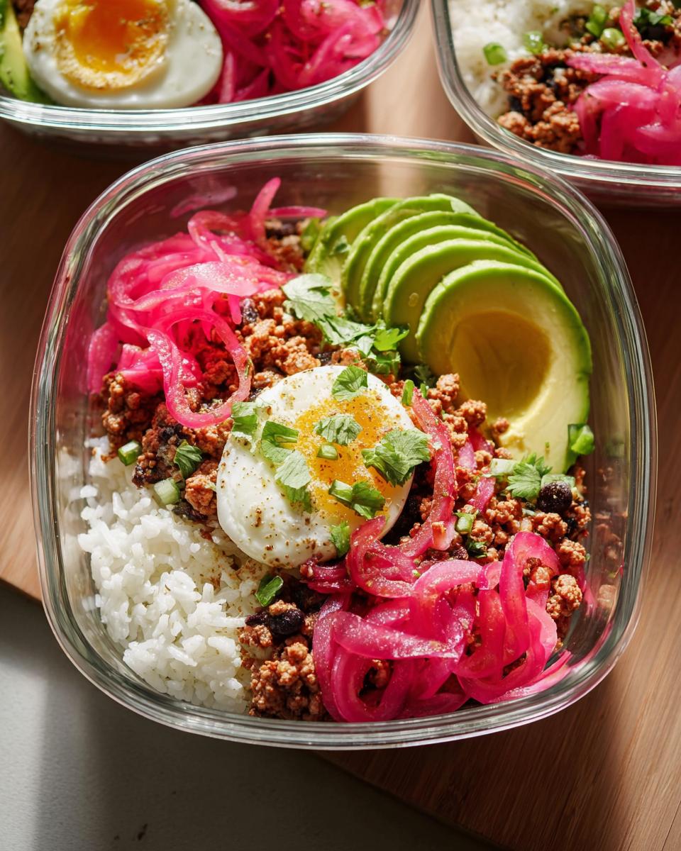 Close-up of a meal prep rice bowl with white rice, seasoned ground meat, pickled red onions, sliced avocado, and a perfectly cooked egg.