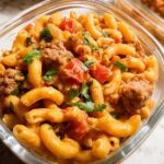 Close-up of a glass container filled with delicious pasta meal prep, featuring elbow macaroni, ground meat, and tomatoes in a creamy sauce, garnished with parsley.