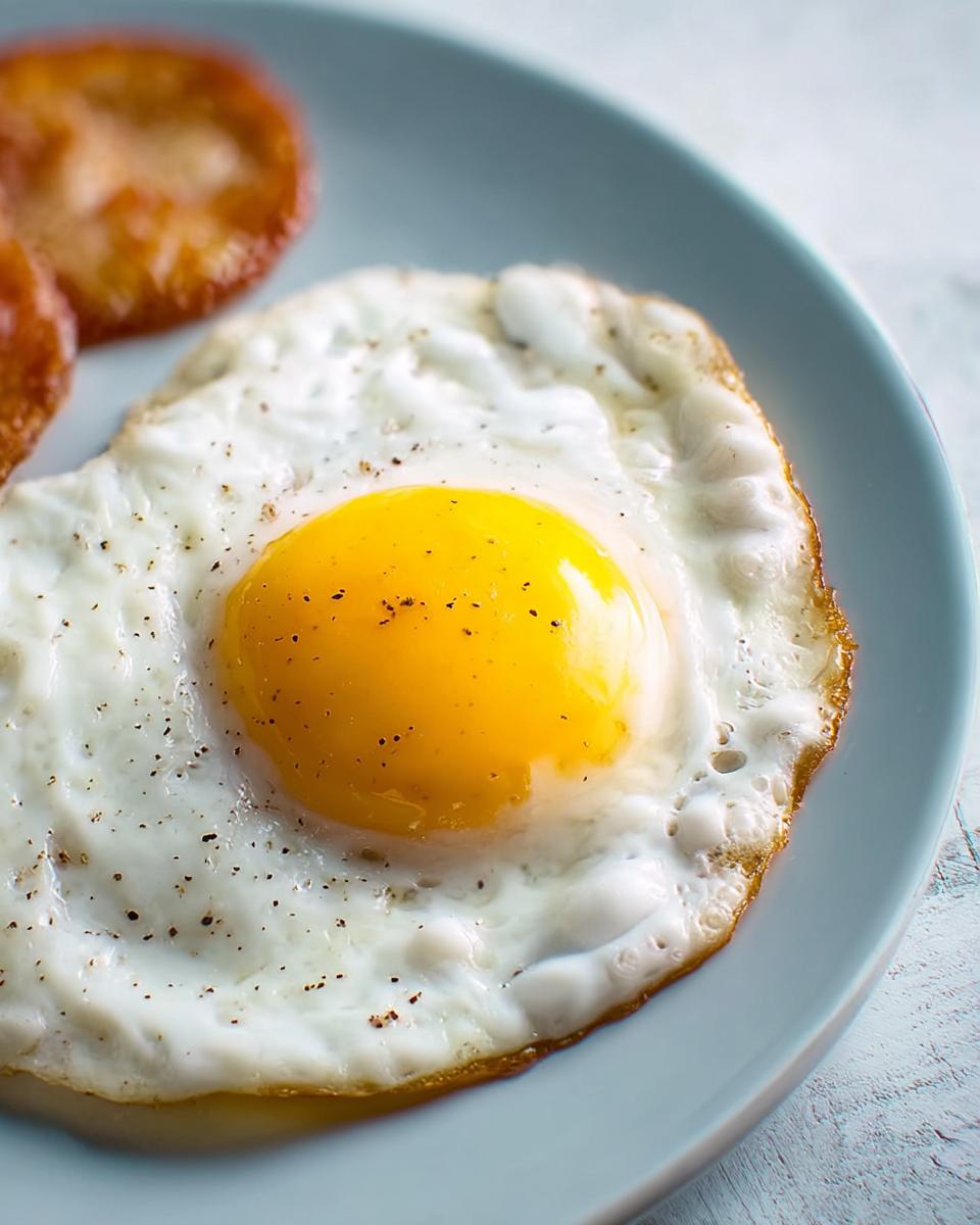 A perfectly fried egg with a bright yellow yolk, seasoned with black pepper, served on a light blue plate.