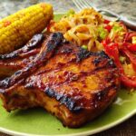 A perfectly cooked pork chop recipe, glazed and grilled, served with corn on the cob and a side of sautéed peppers and onions.