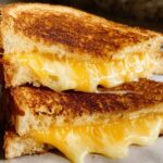 Two halves of a perfectly grilled cheese sandwich, with gooey melted cheese spilling out.