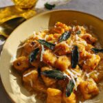 A close-up of pumpkin gnocchi pasta recipe served in a yellow bowl, topped with sage and parmesan cheese.
