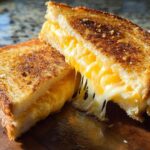 Close-up of a restaurant-style grilled cheese sandwich, cut in half, with melted cheese oozing out.