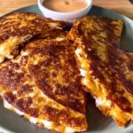 Golden-brown quesadillas filled with melted cheese, served with a side of dipping sauce, perfect for Taco Tuesday.