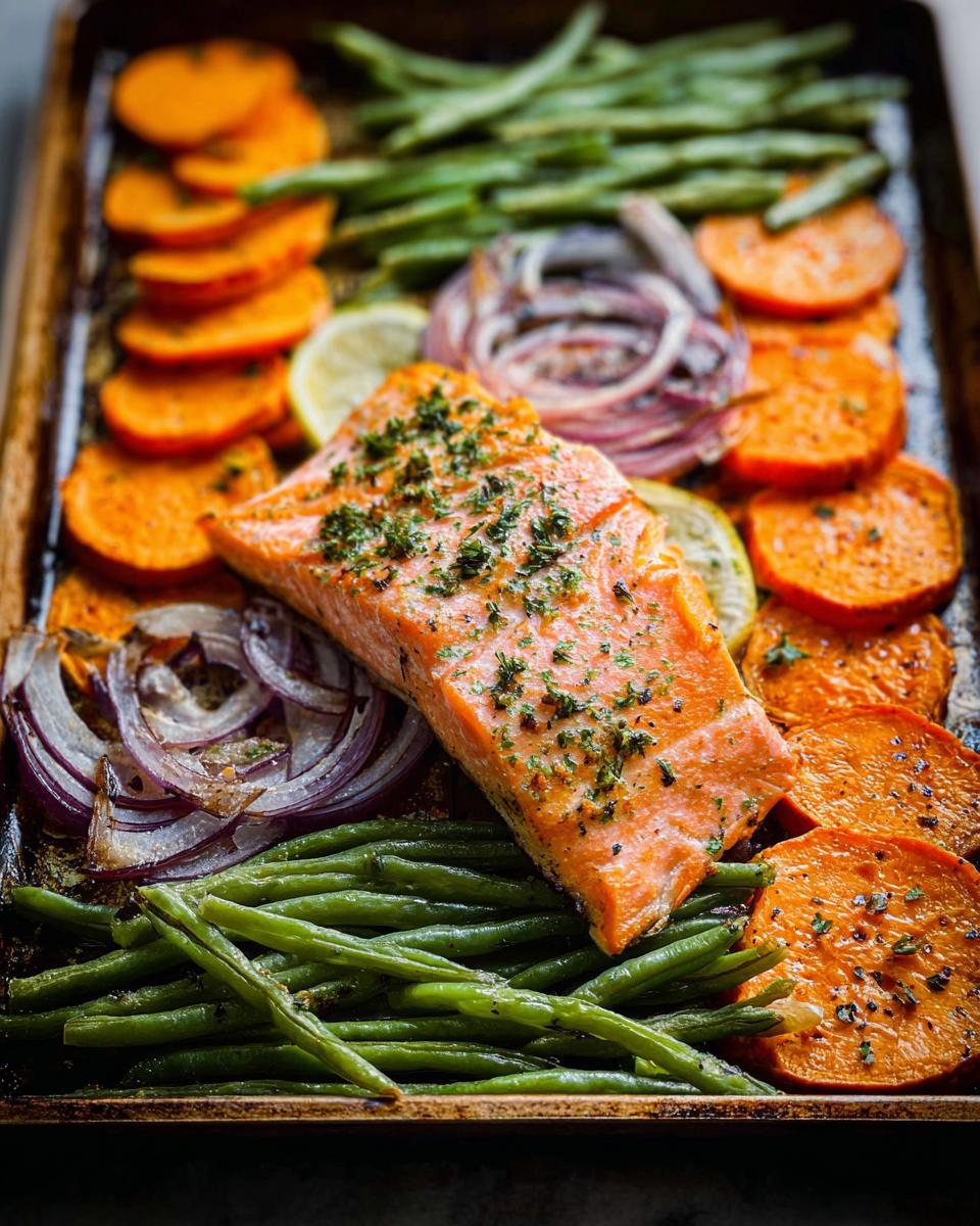A perfectly cooked salmon fillet on a sheet pan with roasted sweet potato slices, green beans, and red onion, ideal for salmon recipes meal prep.