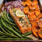 A perfectly cooked salmon fillet with green beans, sweet potatoes, and red onion on a baking sheet, ideal for salmon recipes meal prep.