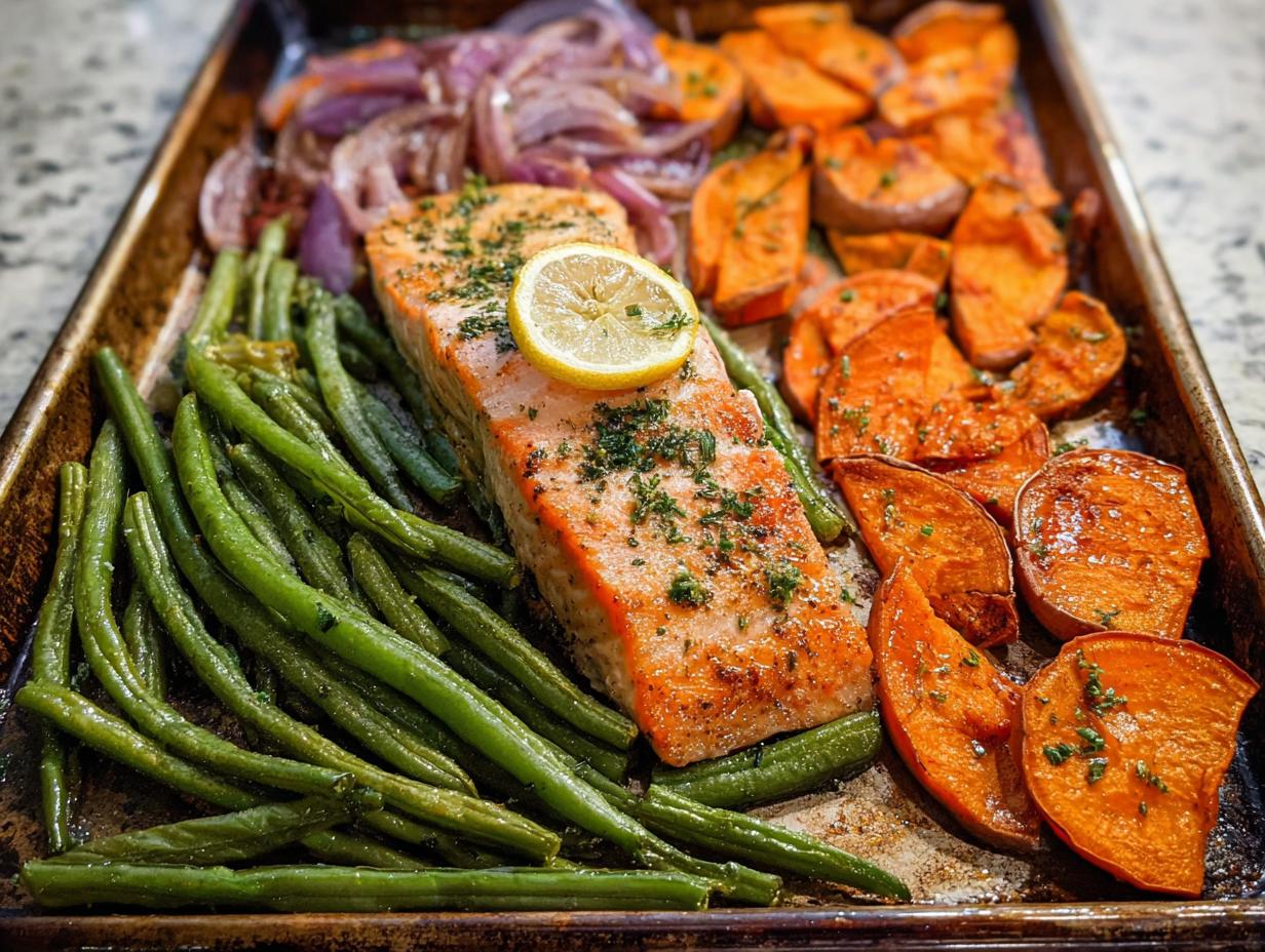 A perfectly cooked salmon fillet with green beans, sweet potatoes, and red onion on a baking sheet, ideal for salmon recipes meal prep.