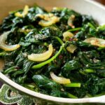 Close-up of sautéed spinach with onion slices and red pepper flakes, a simple side dish from 20-Ingredient Veggie Sides Recipes.