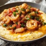 A close-up of shrimp and grits, featuring plump shrimp in a savory sauce over creamy grits, garnished with green onions.