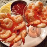 Two martini glasses filled with shrimp cocktail and cocktail sauce, served with lemon slices.