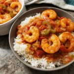 A close-up of a bowl filled with fluffy white rice topped with a rich tomato-based shrimp and vegetable stew. This is one of the best shrimp recipes.