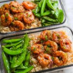 Two meal prep containers filled with brown rice, glazed shrimp, and snow peas, perfect for shrimp recipes meal prep.