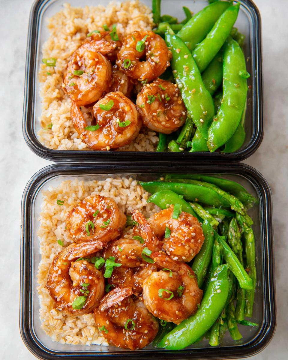 Two meal prep containers filled with shrimp recipes, brown rice, snap peas, and asparagus.