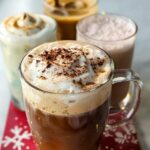 A close-up of a Starbucks drink with whipped cream and cocoa powder, with other Starbucks drinks recipes in the background.