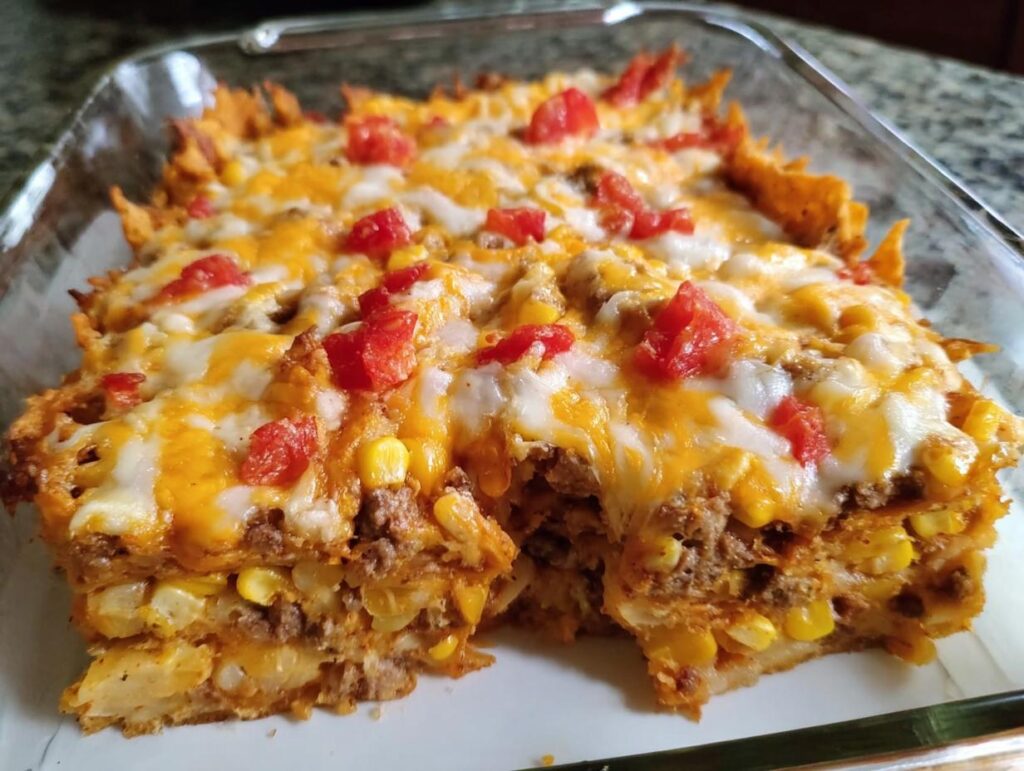 A close-up of a cheesy Taco Tuesday casserole with layers of ground beef, corn, and tomatoes.