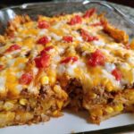 A close-up of a cheesy Taco Tuesday casserole with layers of ground beef, corn, and tomatoes.