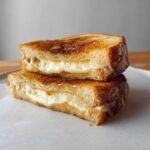 Two halves of a perfectly grilled cheese sandwich stacked on a white plate, showcasing melted cheese.