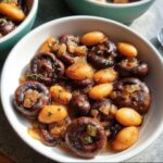 A close-up of a bowl filled with a veggie sides recipe featuring mushrooms, baby potatoes, and onions in a savory sauce.
