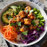 A vibrant bowl of Bang Bang Salmon Bites, served with rice, avocado, edamame, shredded carrots, and red cabbage.