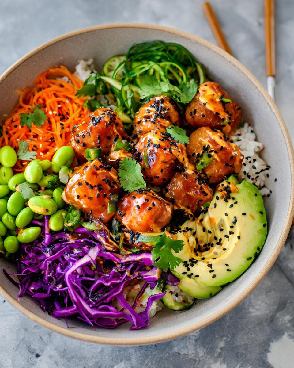 A vibrant bowl overflowing with Bang Bang Salmon Bites, rice, avocado, edamame, shredded carrots, and red cabbage.