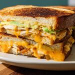 A close-up shot of a stacked CHICKEN AVOCADO MELT SANDWICH with melted cheese oozing out.