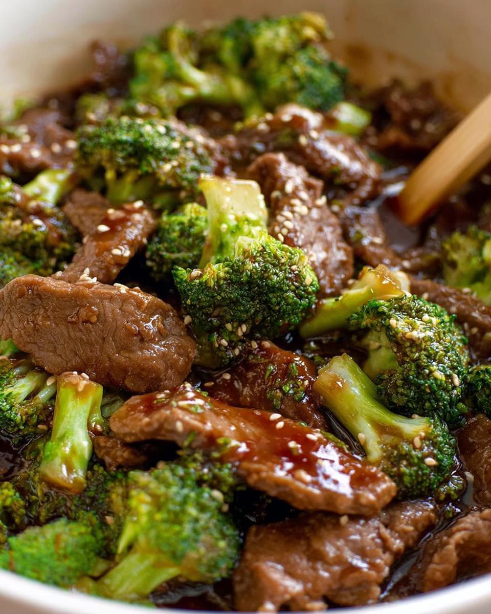 Close-up of tender slices of Chinese beef and broccoli florets coated in a glossy sauce, sprinkled with sesame seeds.