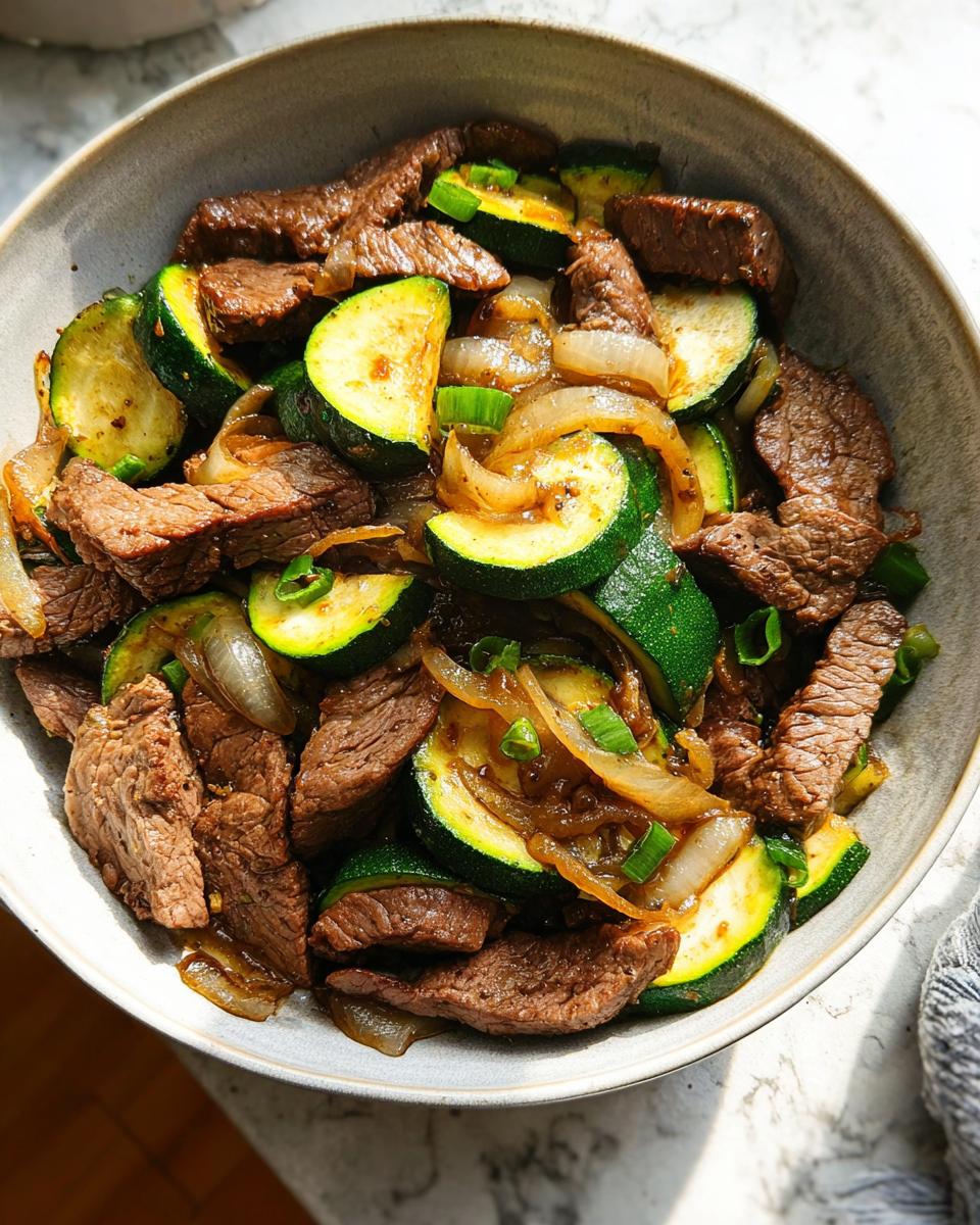 A close-up overhead view of a Cozy Grilled Steak Bowl with Zucchini, featuring sliced steak, zucchini rounds, and onions.