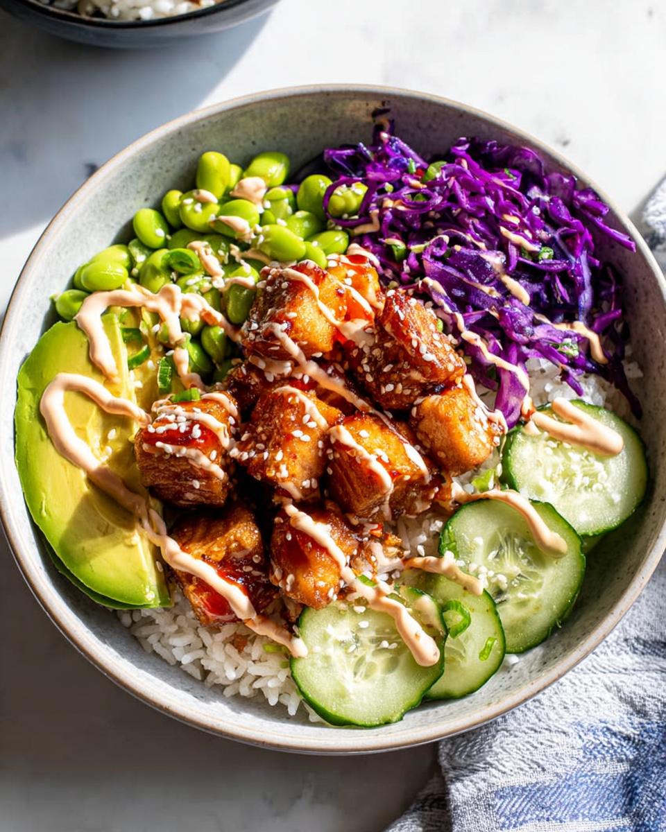 Close-up of a Crispy Salmon and Rice Bowl with avocado, edamame, cabbage, and cucumber, drizzled with sauce.
