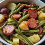 Close-up of a white bowl filled with Crockpot Kielbasa and Green Beans, featuring sliced kielbasa, tender green beans, and chunks of potato.