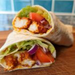 Two Crunchy Crispy Air Fryer Chicken & Mozzarella Wraps filled with lettuce, tomato, and red onion on a wooden board.